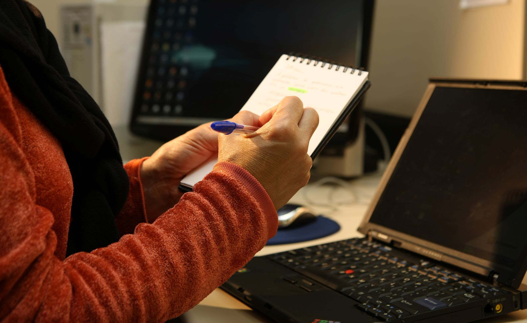 Mulher fazendo anotações em bloco diante de notebook